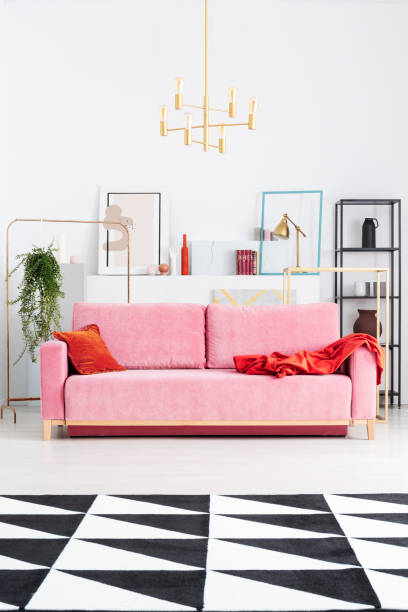 istock Gold lamp above pink couch in white apartment interior with patterned carpet and posters. Real photo 1091285468