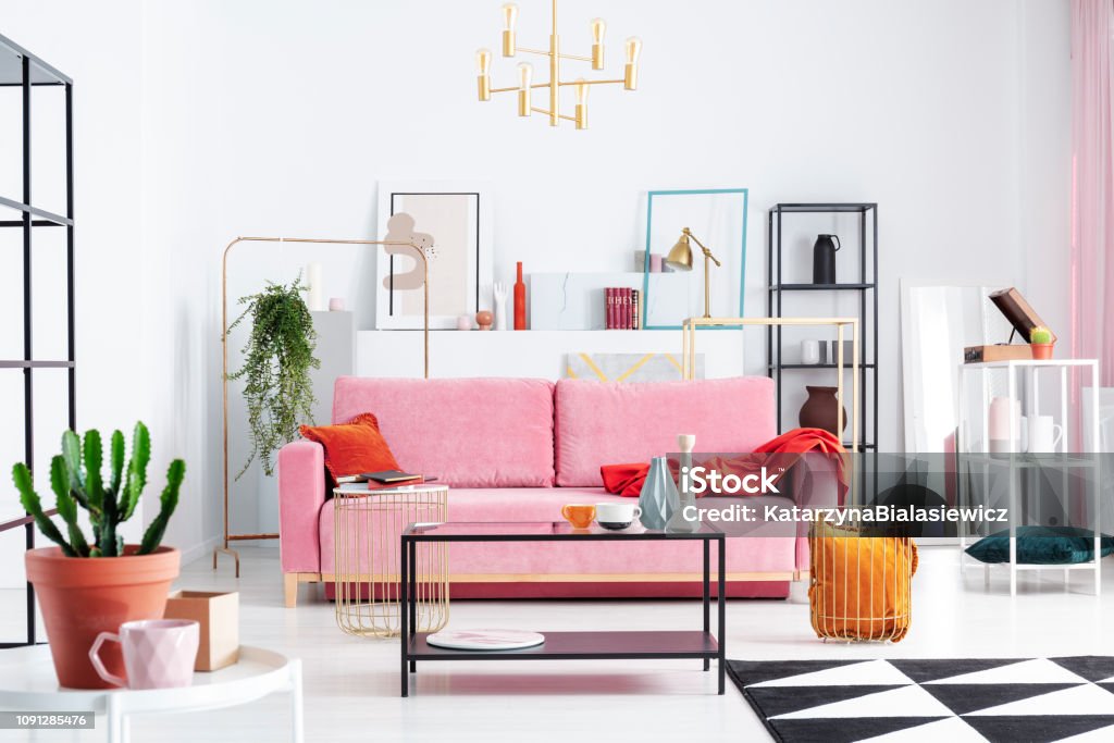 Patterned carpet and pink couch in white apartment interior with posters and lamp above table. Real photo Apartment Stock Photo