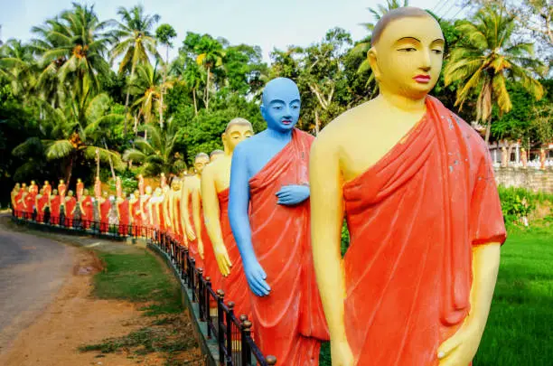 Statues of monks standing in a row, in one of the Buddhist temples of Sri Lanka. Among the statues is a statue of a monk, painted blue.