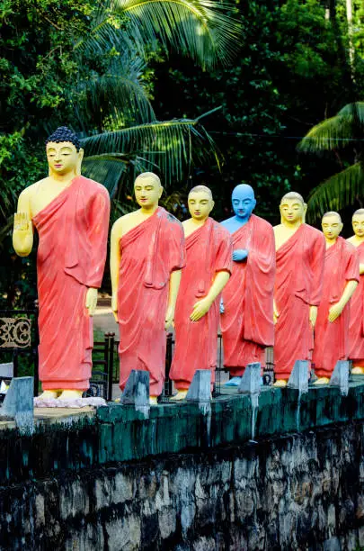 Statues of monks standing in a row behind the Buddha in one of the Buddhist temples of Sri Lanka.