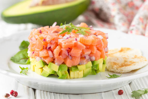 salmon tartare with red onion, avocado, arugula, bread toast. beautiful snack, dietary food, appetizer for christmas holiday. on white wooden background - tartar sauce imagens e fotografias de stock