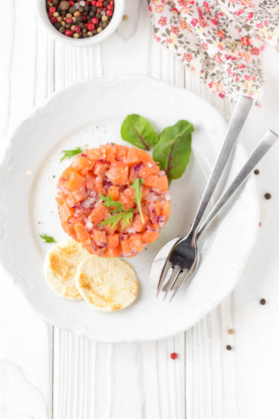 Salmon tartare with red onion, avocado, arugula, bread toast. Beautiful snack, dietary food, appetizer for Christmas holiday. On white wooden background stock photo