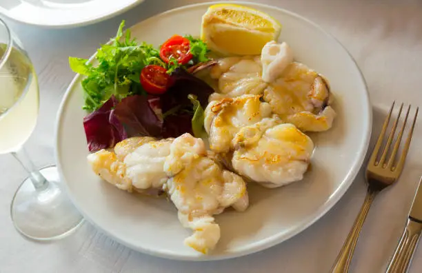 Appetizing baked monkfish served with lemon and garnish of fresh vegetable