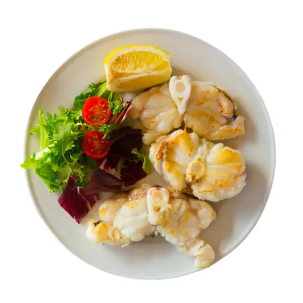 Top view of baked monkfish with fresh greens, cherry tomatoes and lemon. Isolated over white background