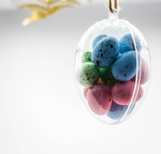 Multi-colored Easter eggs hang in a glass transparent egg bauble on white background.