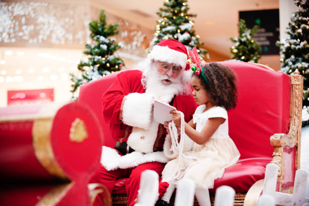 Shopping Christmas with family and Santa Claus at Shopping Mall Multi-Ethnic family shops at Shopping Mall during Christmas Time with Santa Claus. Santa Claus and girl are shopping with digital tablet. Santa and girl is looking at the digital tablet. Santa Claus has a beautiful expression on his face. Photo was taken in Quebec Canada. santa claus photos stock pictures, royalty-free photos & images