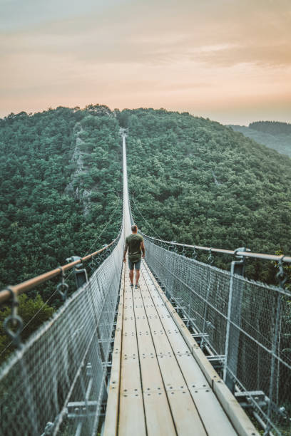 It's hard to look back when you've seen so much Photo of young Man walking on a hanging bridge in Germany during the summer day, Geierlay, The longest pedestrian bridge in Germany, suspension swing bridge. Young Man standing alone outdoor and admiring view Travel Lifestyle concept with rope bridge background and sunset. people on bridge stock pictures, royalty-free photos & images