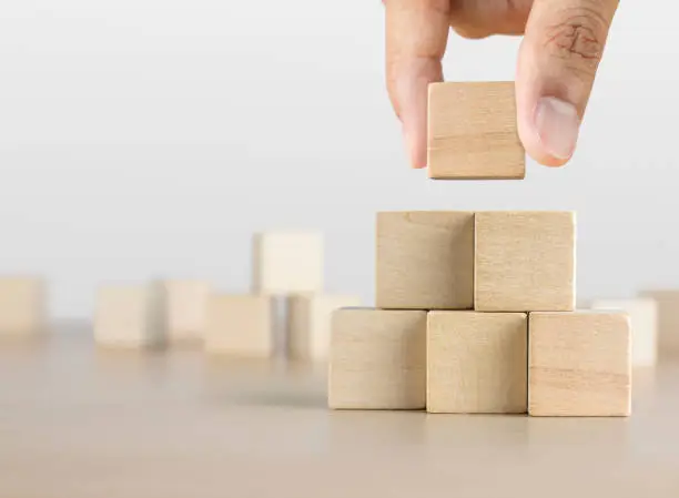 Photo of Hand arranging wooden blocks stacking as a pyramid staircase on white background. Success, growth, win, victory, development or top ranking concept.