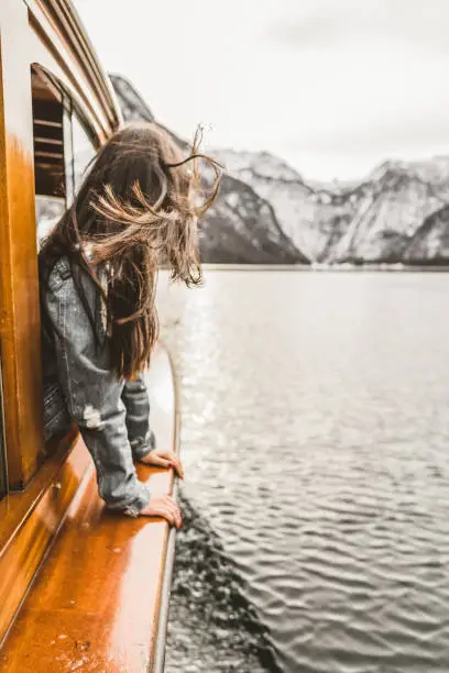 Rear view of young woman looking at view at Traditional passenger boat gliding on Lake  Königssee- Bavaria with Watzmann mountain in the background on a beautiful sunny day in fall, Berchtesgadener Land, Bavaria, Germany. District of the German state of Bavaria, near the Austrian border. National Park.