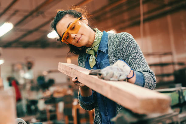 istock Female worker processing wooden beam wearing protective gloves and glasses. 1091345932