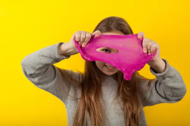 Girl plays with slime on yellow background, portrait. Fun experiments.