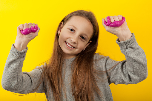 Child girl is holding a toy slime. Portrait on a yellow background.