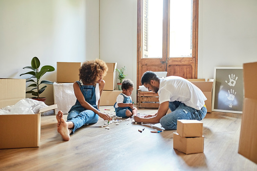 Parents and daughter drawing while sitting on hardwood floor. Family of three is moving into new house. They are wearing casuals.