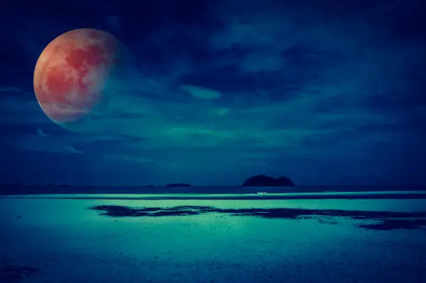 Beautiful fantasy tropical beach of seascape in night. Attractive red super moon or blood moon on dark sky with cloud. Serenity nature background. Vintage filter effect. The moon taken with my camera.