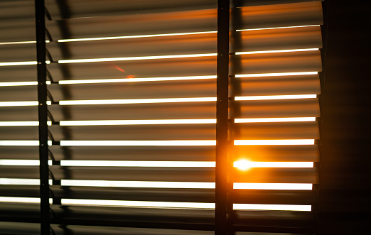 Opened venetian plastic blinds with sunlight in the morning. White plastic window with blinds. Interior design of living room with window horizontal blinds. Window slatted shades made of plastic.