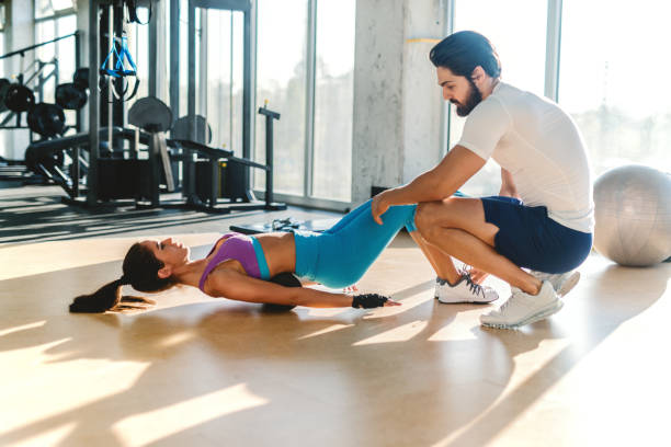 istock Slim Caucasian sporty woman with ponytail doing exercises while personal trainer crouching next to her and helping her. 1091373456