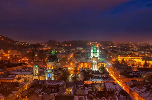 Aerial panoramic view of Dominican Monastery, Dormition Church, Korniakt Tower and old quarters in historical city center at night, Lviv, Ukraine. UNESCO world heritage site. Night winter cityscape.