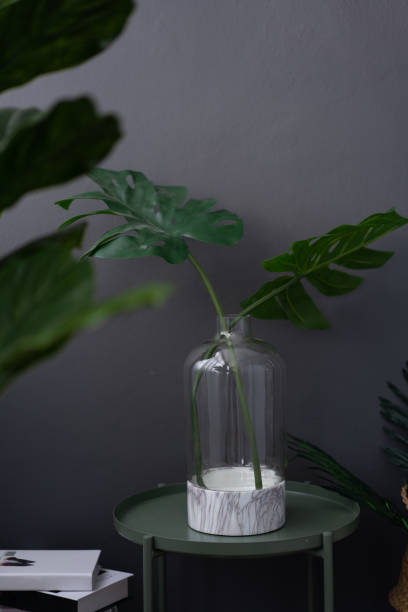 istock Isolated  glass vase with white marble ceramic base on green metal side table in artificial plants and stack books scene on gray painted wall background / object isolation / interior design scene 1091380302