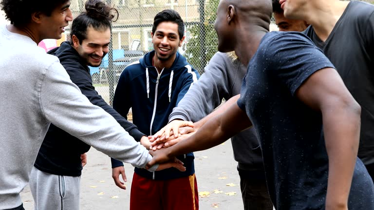 Handheld shot of multi-ethnic team stacking hands on street. Happy soccer players are talking while playing. They are wearing sports clothing.