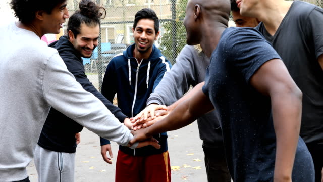 Handheld shot of multi-ethnic team stacking hands on street. Happy soccer players are talking while playing. They are wearing sports clothing.