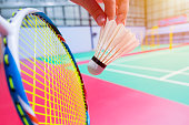 close up hand hold serve badminton shuttlecock with blur badminton court background