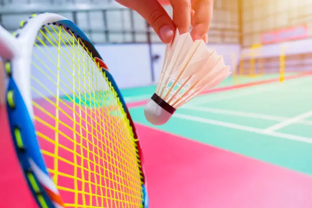 Photo of close up hand hold serve badminton shuttlecock with blur badminton court background