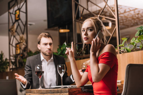 istock dissatisfied man looking at girlfriend talking on smartphone during dinner 1091397840