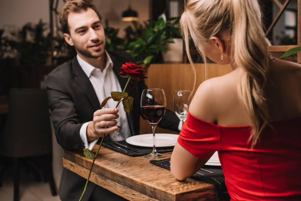 istock cheerful man giving red rose to girlfriend while sitting in restaurant 1091397874