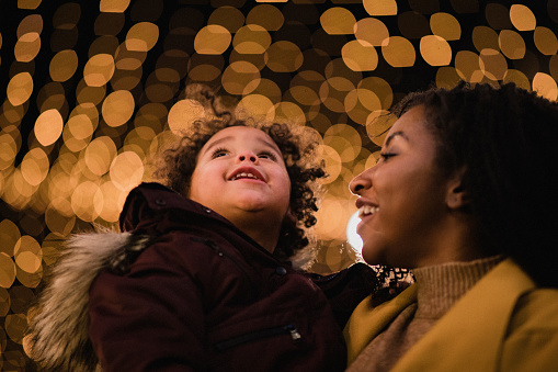 A close-up shot of a mother and her daughter standing under the Christmas lights, the young girl is looking up in awe.