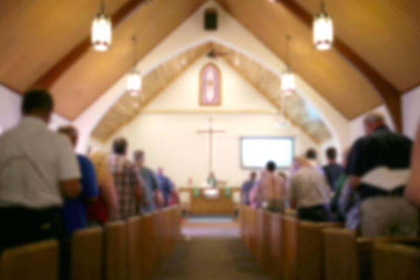 Blurred Photo of the Iterior of a Church Sanctuary with Congregation, Pastor, and a Large Cross Visible A blurred photo of the inside of a church sanctuary that is filled with people in the pews, and the pastor stands under a large cross at the altar. protestantism stock pictures, royalty-free photos & images