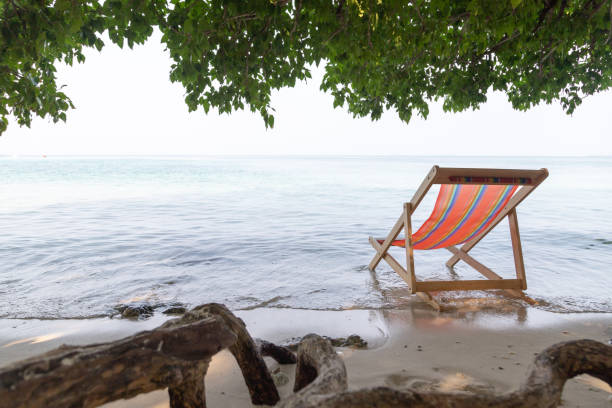 The orange beach chair is under the tree with sea in background stock photo