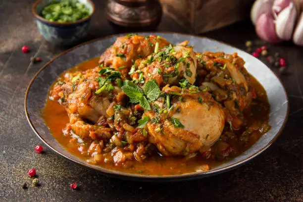 Chicken in tomato sauce with herbs and onions, cilantro parsley mint, traditional Oriental dish chakhokhbili, delicious homemade food. On dark background