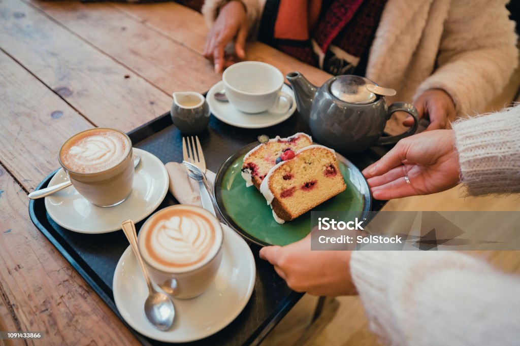 Coffee and Cake with Friends Close-up of a unrecognisable waitress placing a tray with coffee and cake on a table. Cake Stock Photo