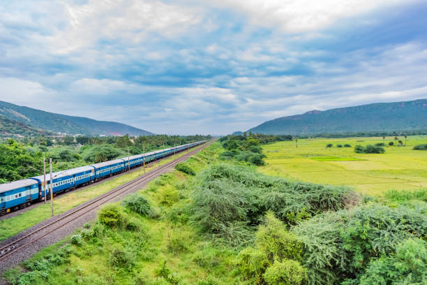 awesome view of indian railway running on track goes to horizon in green landscape under blue sky with clouds. stock photo