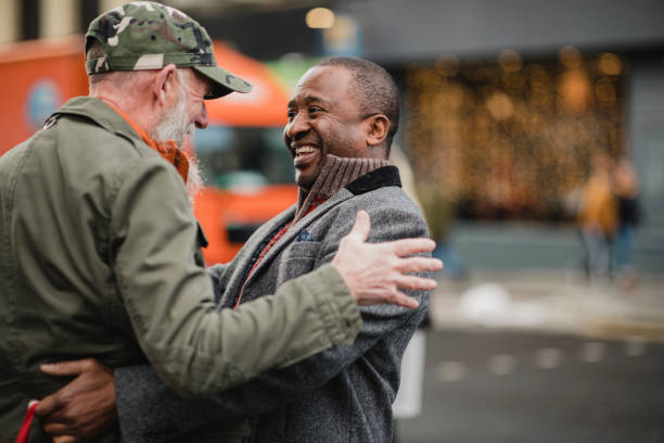 Fancy Seeing You Here! Two senior men have bumped into each other in the city and are greeting each other with a friendly hug. street friends stock pictures, royalty-free photos & images
