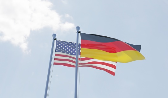 USA and Germany, two flags waving against blue sky. 3d image