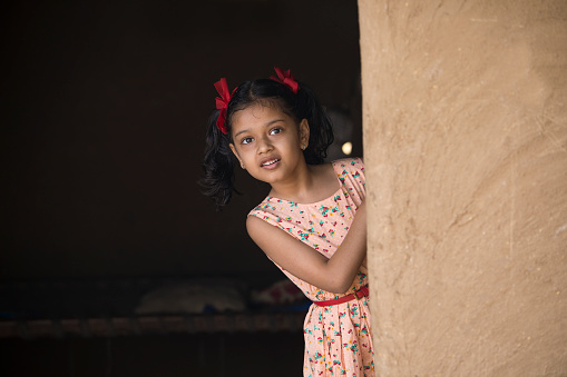 Little Indian girl peeking out of her house in village