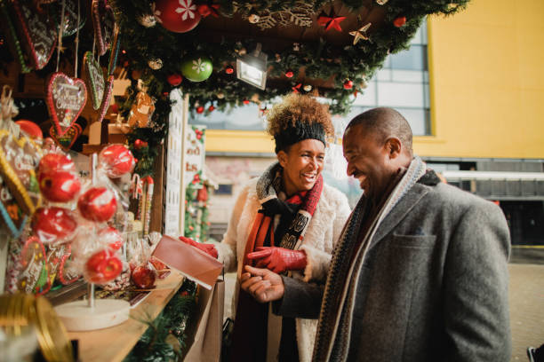 Looking at a Christmas Market Stall Mature couple looking at a Christmas market stall in a city centre. They are talking and laughing while holding a gift. christmas market photos stock pictures, royalty-free photos & images