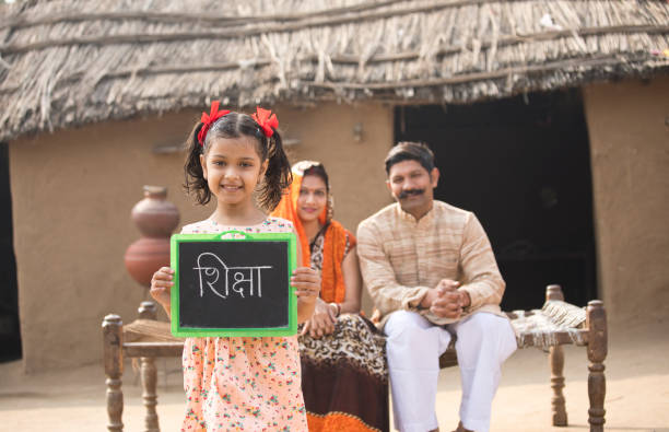 Parents with daughter holding slate at village Happy Indian parents with daughter holding slate while sitting on traditional bed in village happy indian young family couple stock pictures, royalty-free photos & images