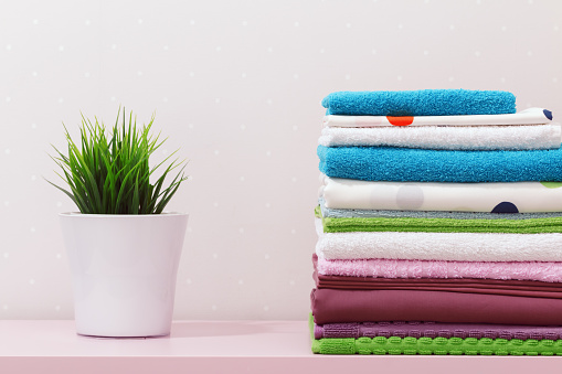 On the dresser there is a stack of clean ironed bed linen, folded multi-colored towels and a home plant stands.