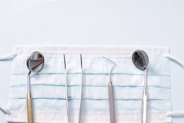 instruments de base de dentiste : deux miroirs, sonde dentaire et pince à épiler se trouvant sur un masque médical sur la lumière de fond gris. - dentist mirror orthodontist carver photos et images de collection