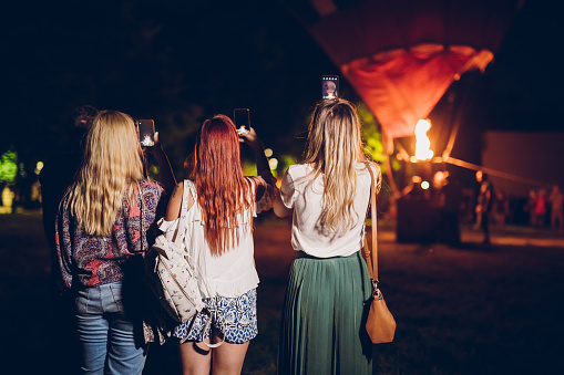 Group of four friends taking photos of hot air balloon at a music festival