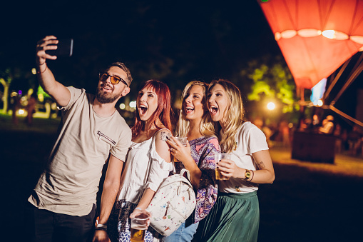 Group of four friends making selfies close to hot air balloon on a music festival