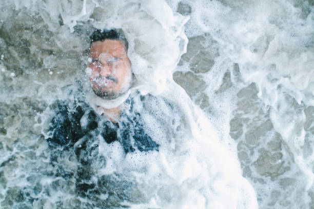 Man Covered in Water A man covered in water as a wave hits him while laying on the beach. baptism photos stock pictures, royalty-free photos & images