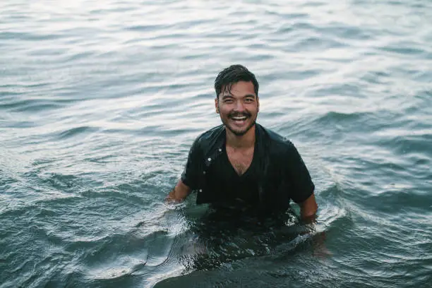 A man in wet clothes smiles while swimming in the ocean.