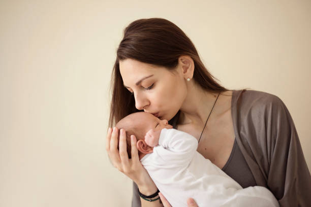 mother kissing newborn son at grey background. portrait of woman and little baby love - mother baby new kissing imagens e fotografias de stock