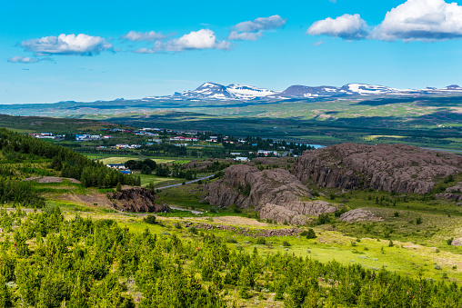 Town of Fellabaer in Fljotsdalsherad municipality of Eastern Iceland is in the border of Lagarfljot lake, rocky hills with pine forest are at foreground and mountain chain is at background
