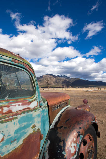 Taos, NM: Rusty Old Blue Pickup Truck, Taos Mountains Background Taos, NM: A beautiful old rusty blue-green pickup truck in the foreground, with a wide prairie in the middle ground and Taos Mountains in the background. Beautiful sunny blue sky with clouds. Vibrant colors. distressed rusty vintage pickup truck close up detail stock pictures, royalty-free photos & images
