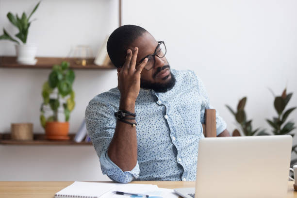 serio uomo d'affari africano premuroso seduto alla scrivania - frustration computer men emotional stress foto e immagini stock