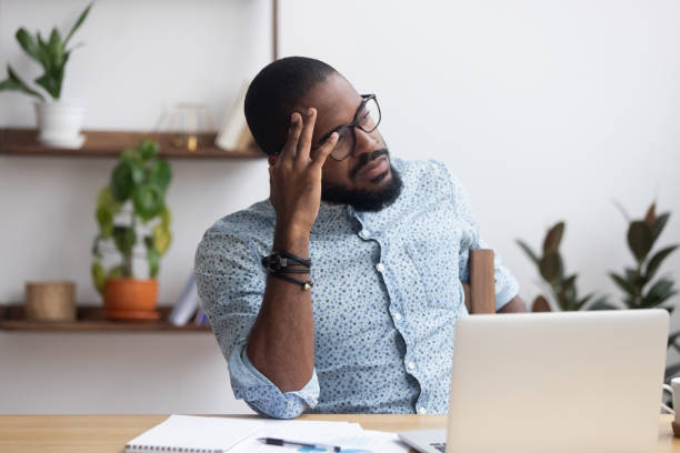 Serious thoughtful african businessman sitting at desk Serious african millennial businessman thinking cogitating about business issues. Frustrated black entrepreneur searching problem solution sitting alone on chair at modern office desk looking away frustration stock pictures, royalty-free photos & images